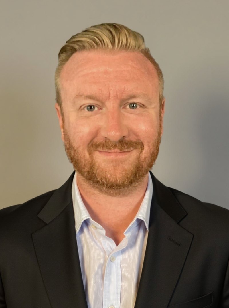 Mike Paul in a dark suit, photographed against a plain studio background